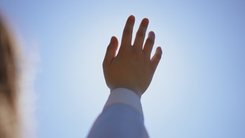 A hand is reaching upwards against a bright and clear blue sky, symbolizing hope, dreams, and aspirations in life