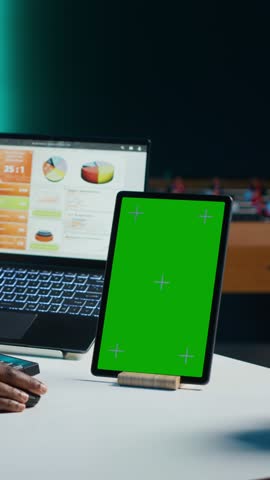 Vertical video Freelancer using isolated screen tablet, analyzing statistical charts on laptop in living room. Remote employee checking business revenue numbers on chroma key electronic device