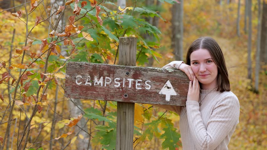 Teen Girl Leans Against Campsite Sign on a Hiking Trail on the Forest in the Fall