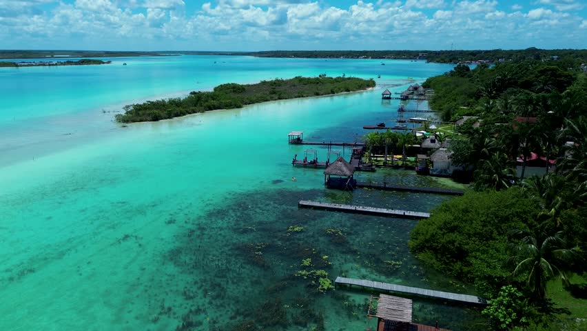 Drone aerial pan of forest sandbar island with hotel resort restaurant huts on boardwalk jetty pier in Bacalar village town lagoon lake Mexico Quintana Roo travel holidays