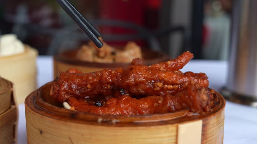 Close up shot of a traditional dim sum dish, featuring braised chicken feet in rich and spicy fermented black bean sauce, served in bamboo steamer at the restaurant, picked up using chopsticks.