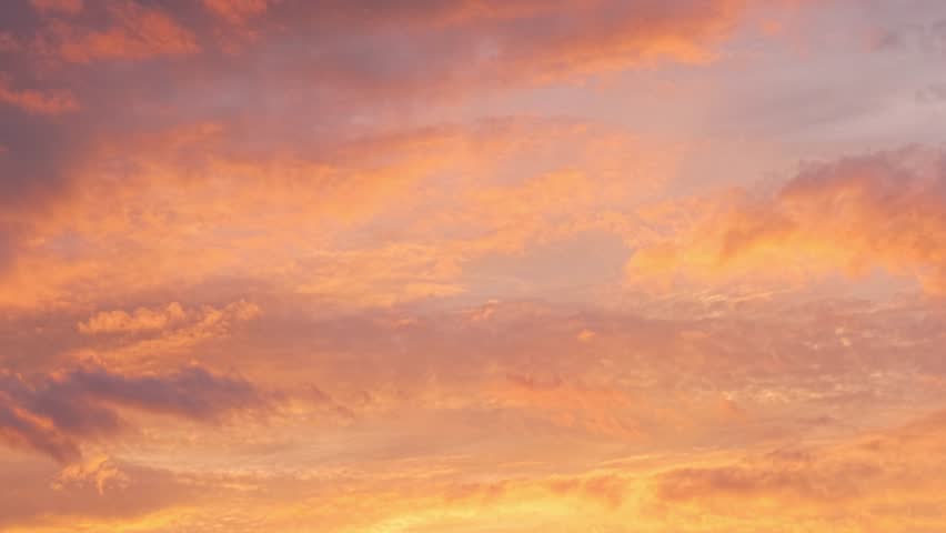 Vibrant orange and pink clouds fill the sky during a serene sunset over the horizon