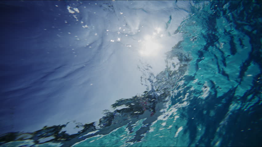 Slow motion underwater shot of waves building up in artificial wavepool, light reflects dynamically in the water, dreamy surfer silhouette
