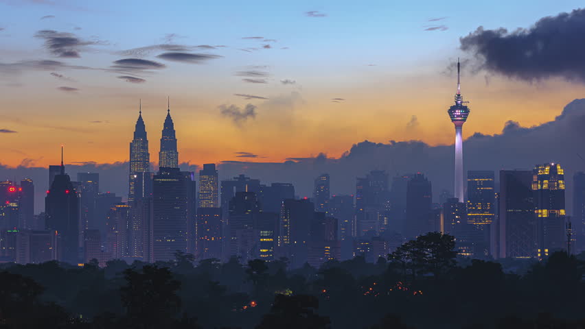 Time lapse: KL cityscape during colorful dawn overlooking the city skyline from afar bright sun and lushes green in the foreground. Kuala Lumpur, Malaysia. Prores 4KUHD 