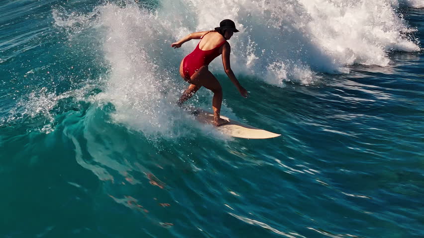 Teen girl surfs the wave. Aerial view of the female surfer riding the wave in the Maldives
