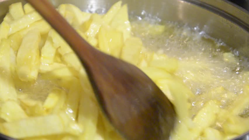 Stirring French Fries With wooden Spatula in fryer pan closeup. Boiling in oil.