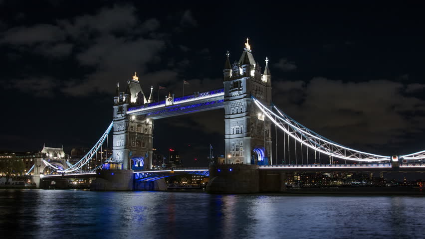4K wide angle night shot of tower bridge with blue neon lights and light trails over smooth river