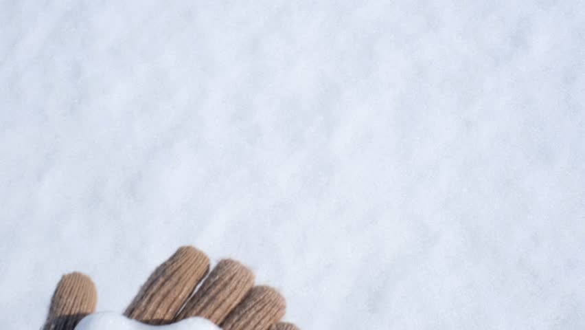 Female hand in brown glove holding heart shaped snowball on white background.