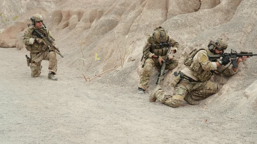 Soldiers in camouflage uniforms aiming with their rifles ready to fire during military operation in the desert