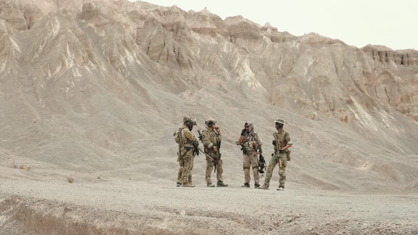 Soldiers in camouflage uniforms aiming with their rifles ready to fire during military operation in the desert