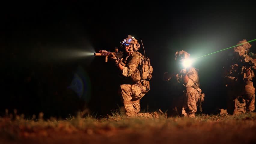 Soldiers in camouflage uniforms aiming with their rifles ready to fire during Military Operation at night