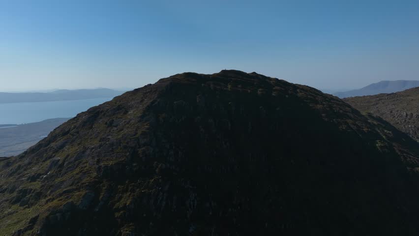 Sugarloaf, Caha Mountains, County Cork, Ireland, September 2024. Drone pulls backwards from the summit of the majestic peak under a clear blue sky with a breathtaking views of surrounding landscape.