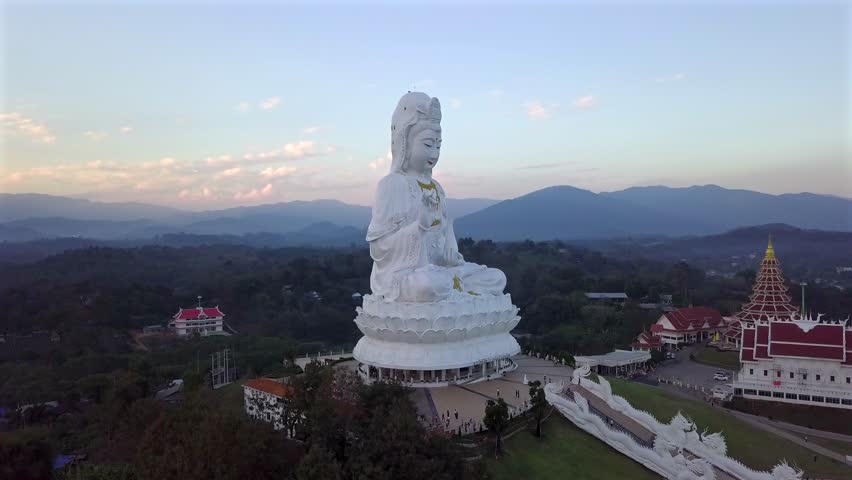 Thailand,Chiang Rai, Wat Huay Pla Kang, Buddha Statu's Drone Footage zooming in,white and pink clouds, hills lying behind the statue.