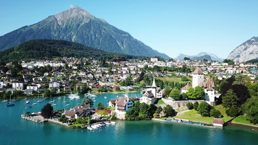 Aerial orbiting revealing the medieval Spiez castle, on the shores of lake Thun - thunersee - , sits beneath the majestic Niesen mountain, Bern, Switzerland