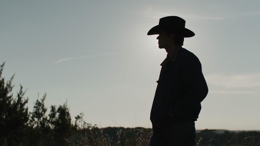 Silhouette of Cowboy Turning While Against a Glowing Sunset.The warm colors of the sky and the cowboy’s silhouette evoke a sense of tranquility and timeless Western charm.