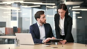 Two co-workers discuss work issues while sitting at workplace in business office. Male manager and female worker reviewing documents, engaged in paper work. talking about the development project - Powered by Shutterstock - Get 15% off with code: PIKWIZARD15
