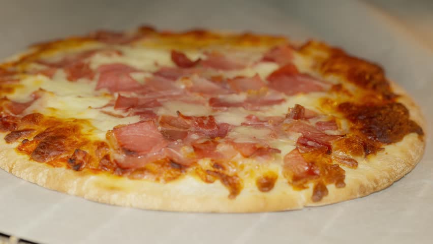 Close-up of a freshly baked pizza featuring crispy ham and melted cheese, set on parchment paper. Perfectly cooked crust adds to the mouthwatering appeal of this classic comfort food.