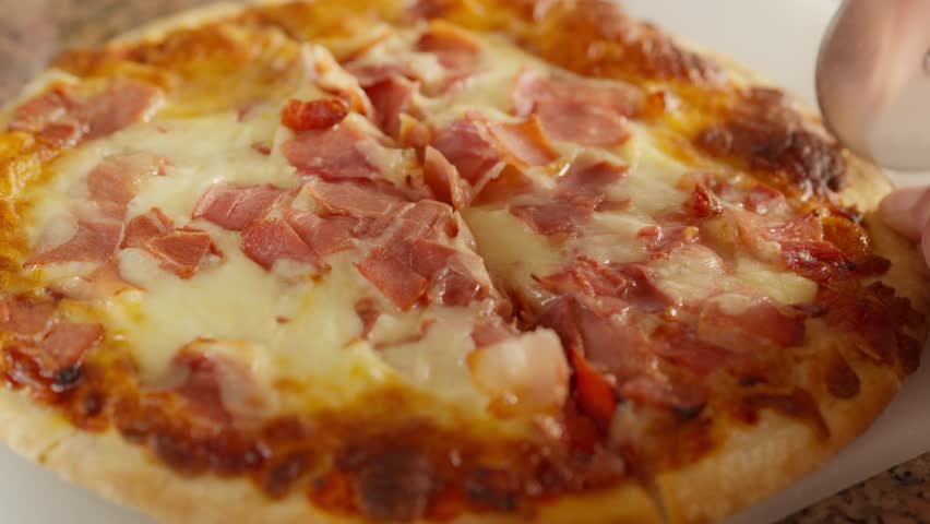 A freshly baked pizza topped with cheese and ham is being sliced. The appetizing look highlights its crispy crust and melted toppings, perfect for casual dining or special occasions.