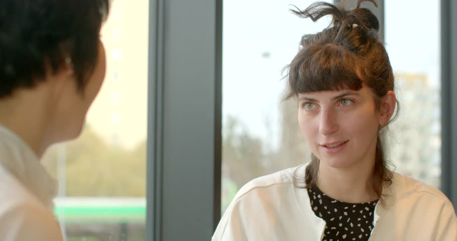 Two professionals engaged in conversation, discussing ideas in a well-lit indoor background.