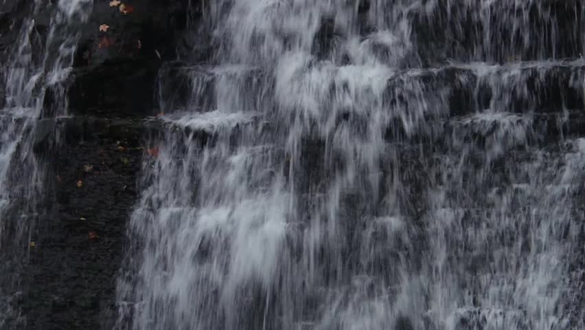 Close-Up of Cascading Waterfall Flowing Over Black Rock With Autumn Leaves