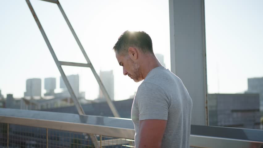 Back view of mature grey athlete male person running on sunny modern urban bridge doing daily cardio routine. Disciplined Caucasian adult man training outdoors for healthy lifestyle in European city