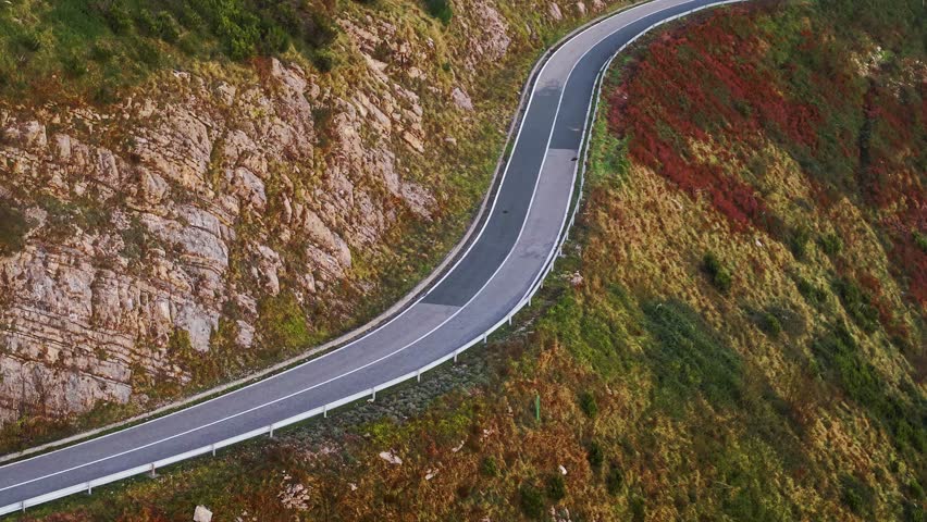 A lone biker speeds through winding mountain roads in Italy on a scenic autumn day