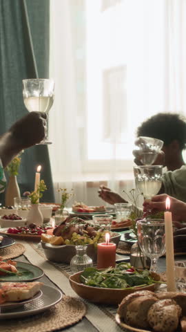 Vertical shot of senior man clinking glasses with unknown relatives while celebrating thanksgiving at festive table, grandson in background