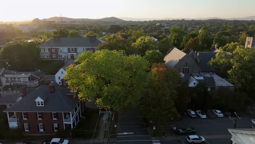 Slow drone flight over street in american town with colorful trees on quaint autumn day. Wide shot in american neighborhood with houses and homes. Sunny fall season. Parking cars in housing area,USA.