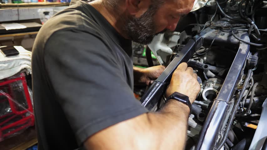 Adult repairman fixing motor of motorbike at workshop. Professional mechanic repairing engine of motorcycle at workplace. Male repairer mending detail of moto at garage. Concept of maintenance service