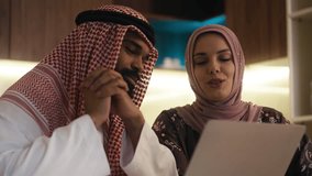 Joyful Arab woman and her husband in traditional wear shop online on a laptop - Powered by Shutterstock - Get 15% off with code: PIKWIZARD15