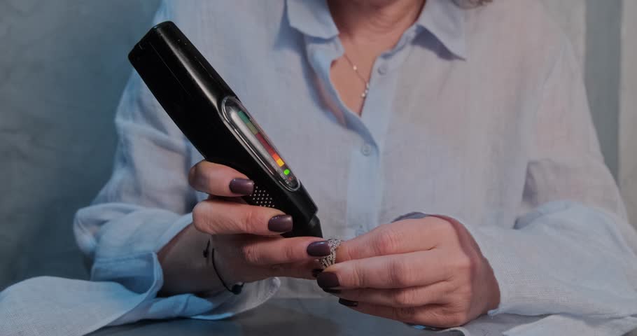 Detailed view of a jeweler using a handheld diamond tester to check the authenticity of a gemstone on a ring
