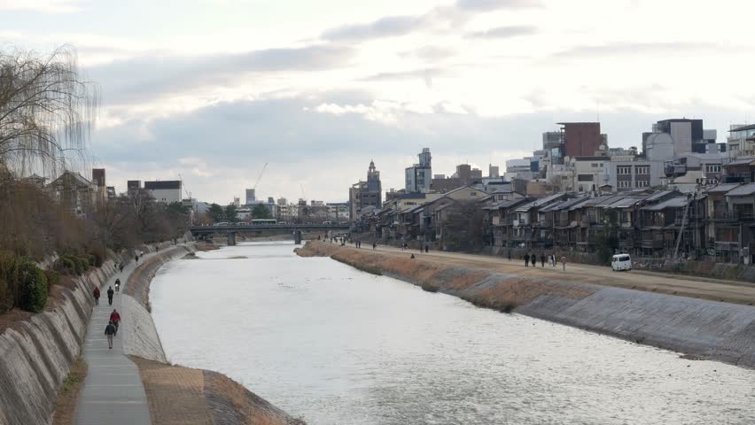landscape view to Kamo gawa river flowing through city center of Kyoto in afternoon winter day time wiht people relax,workout and doing outdoor activity along the riverbank