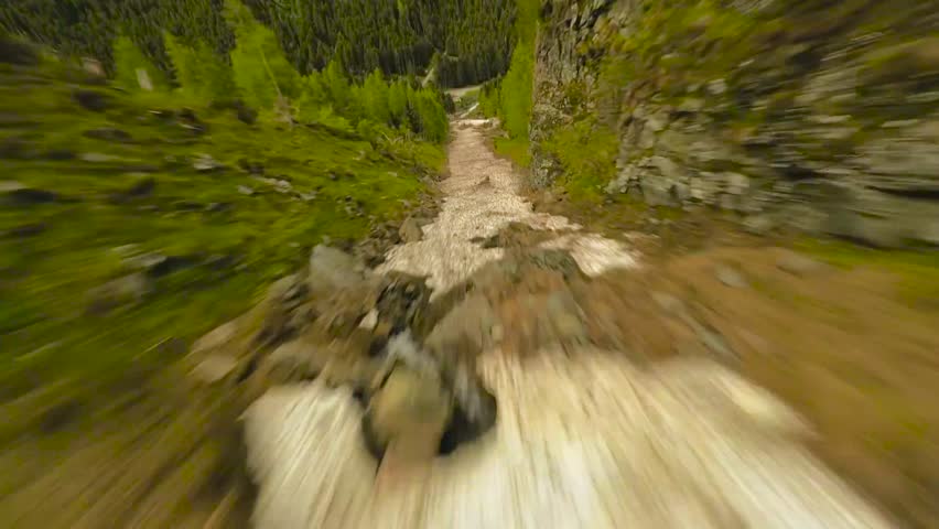 FPV aerial drone flying from high in the mountains between them and close to the ground during a beautiful summer or autumn day. not melted and white snow is in between the mountains.