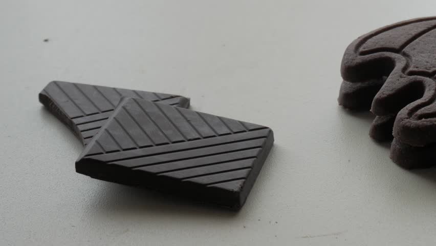 Chocolate squares and a bat-shaped cookie on a white surface, showcasing a spooky treat setup