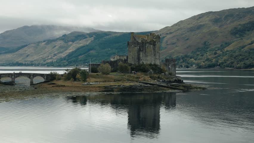 Aerial low orbit view of Eilean Donan Castle in the Scottish Highlands, Scotland, set against a picturesque loch and rugged highland scenery
