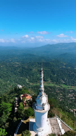 Approaching the stunning the Ambuluwawa Tower Temple with tourists walking by the winding stairs. Top view. Aerial perspective on the green panorama of Gampola Town, Sri Lanka. Vertical video.