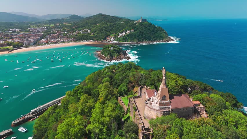 Aerial view of the beautiful coast of San Sebastian town, Basque country, Spain. Flying over the statue of Christ stands watch over magnificent Bay of Biscay, Donostia. Orbit shot