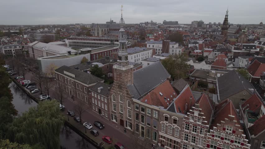 A drone footage of St. Louis Catholic Church (Heilige Lodewijkkerk) and the riverfront buildings on an overcast day in Leiden, Netherlands