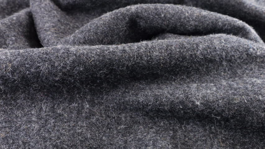Close-up view of the soft folds of textured gray wool fabric rotated on the display case. Textile background on cold weather, warm clothes, comfort, accessories and design theme.