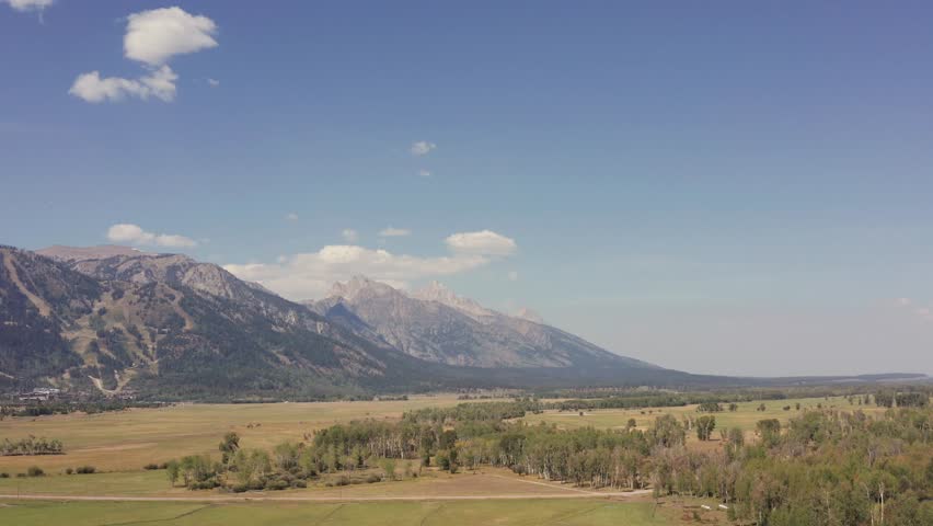 Aerial drone shot of the Grand Tetons from Snake River Ranch in Jackson, Wyoming. Daytime view of the valley looking toward the mountains. Parallax. Shot in 4K.
