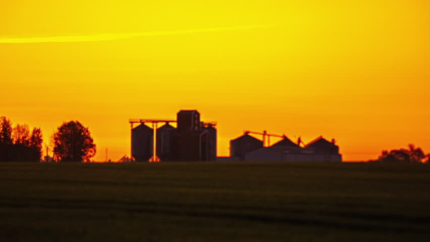Industrial cereal storage containers, golden orange sky sunrise rural landscape