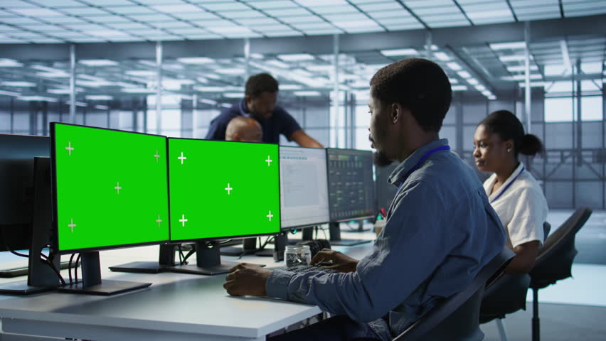 Technician using multi monitor green screen computer setup, working in server farm to optimize it for data processing requirements. Man doing developing on chroma key PC in data center