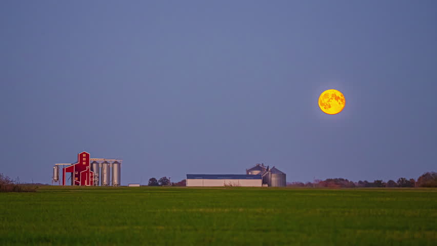 Telephoto timelapse of full moon moonrise over farm and grain elevators