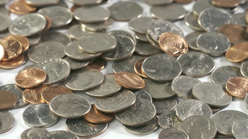 Coins fall onto fall and bounce onto a white surface in slow motion.