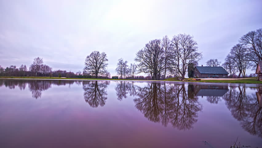 Timelapse captures the beauty of a rural landscape with a tranquil lake and house as it transitions through the four seasons with snow, autumn leaves and frozen lake