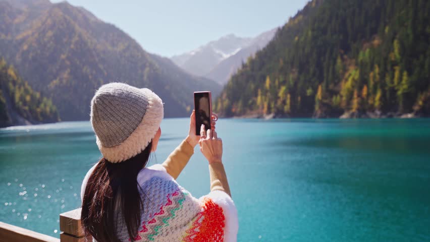 Young female tourist enjoying and taking a photo at beautiful autumn scenery landscape at jiuzhaigou national park in Sichuan, China