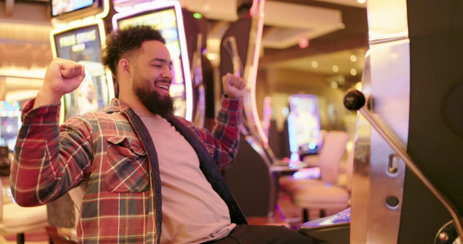 Young African American man is filled with joy as he celebrates a significant win at the casinos vibrant slot machine, showcasing his overwhelming excitement and the sweet taste of victory moment