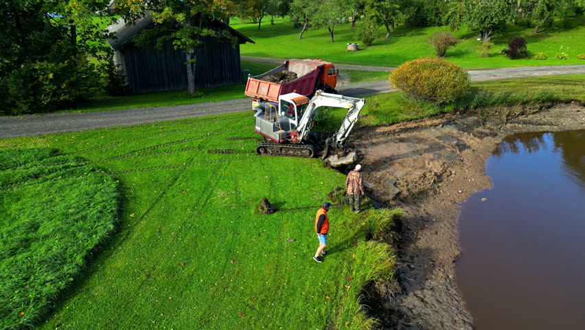 Excavator And Men At Work Digging Field Near Pond. drone shot