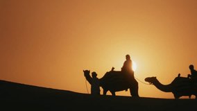 Silhouette of tourists riding camels on top of a dune in a safari desert tour during sunset - Powered by Shutterstock - Get 15% off with code: PIKWIZARD15