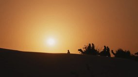 Silhouette of tourists riding camels on top of a dune in a safari desert tour during sunset - Powered by Shutterstock - Get 15% off with code: PIKWIZARD15